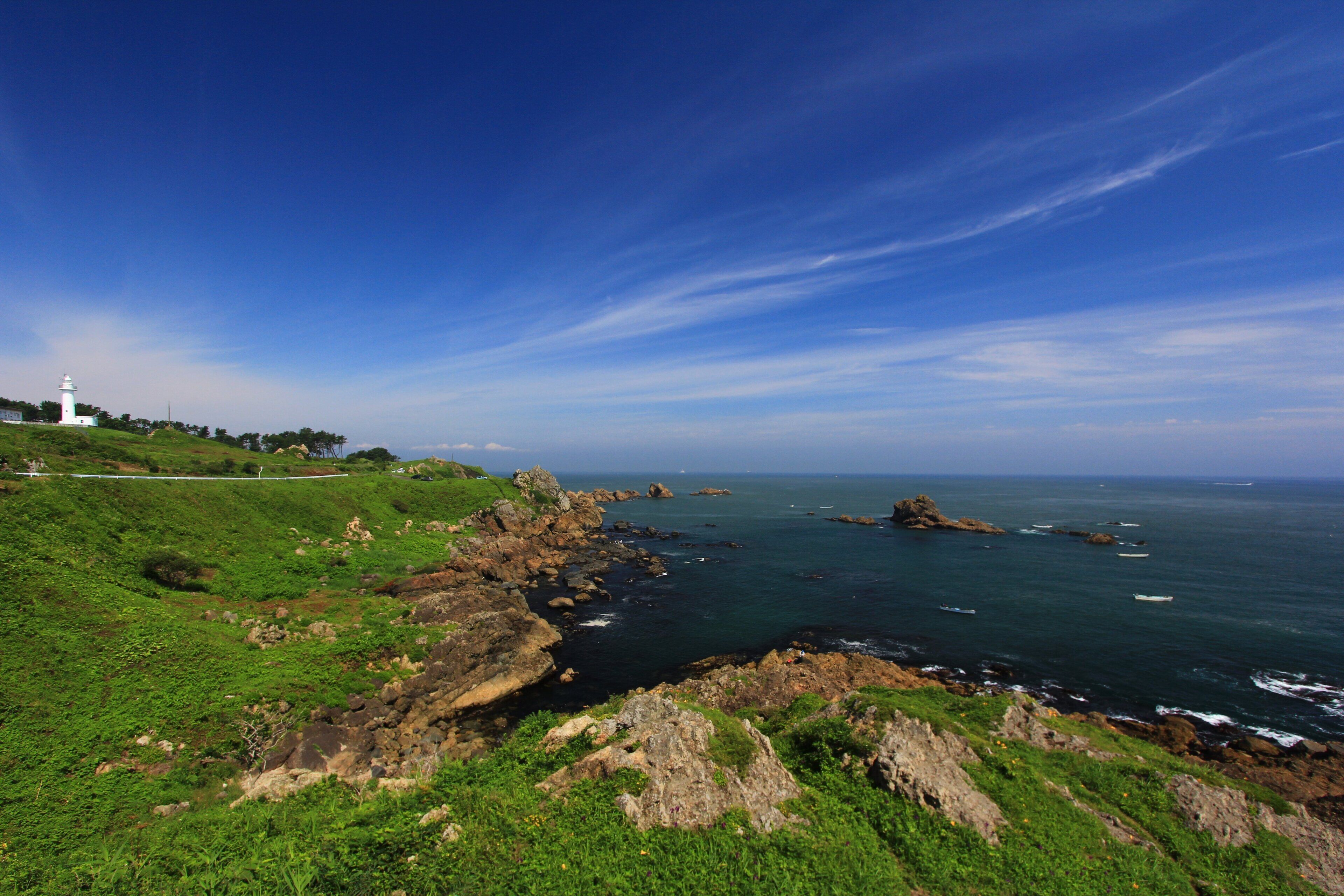 A coastal landscape with a lighthouse, rocky shoreline, and green hills.