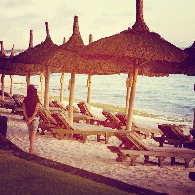 A beach with thatched umbrellas and lounge chairs.