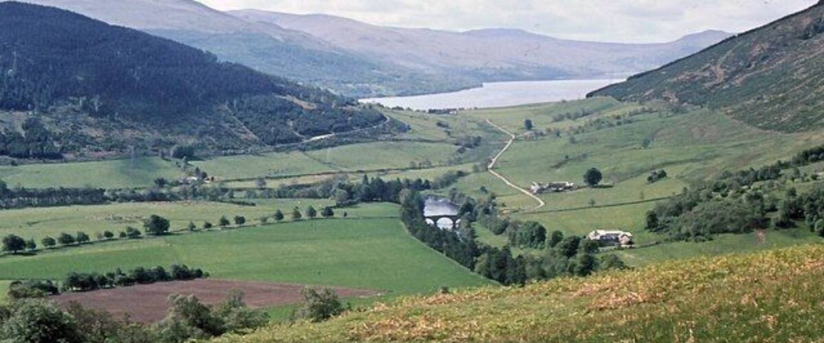 A valley with a lake, rolling hills, and a small house.