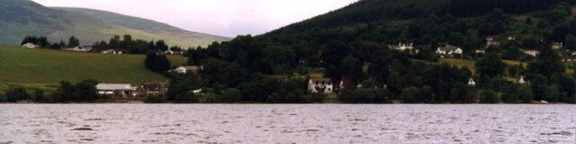 A lake with houses on the shore and hills in the background.