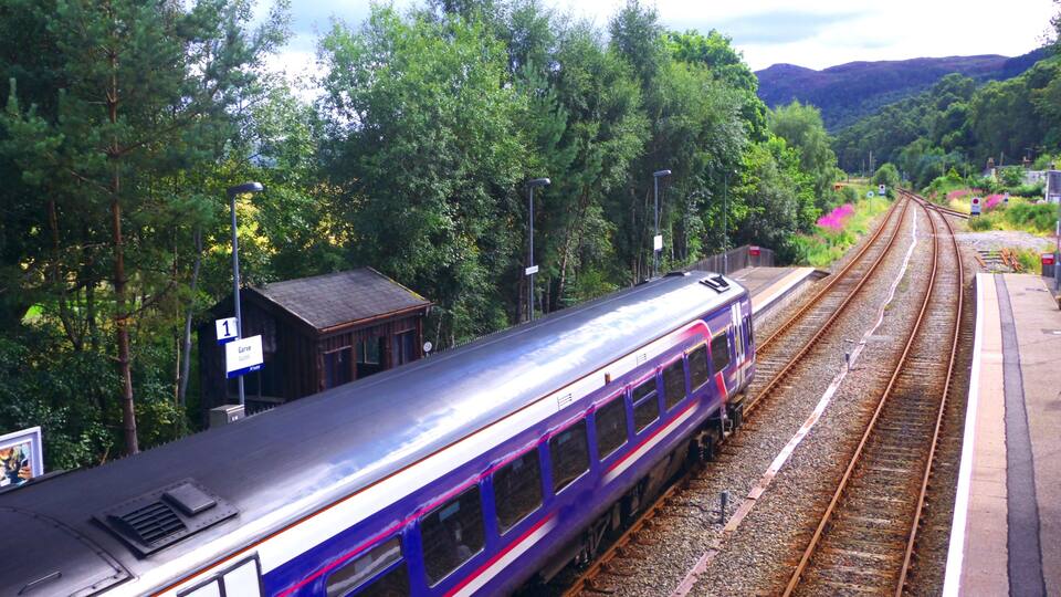 A train on tracks surrounded by lush greenery and hills.