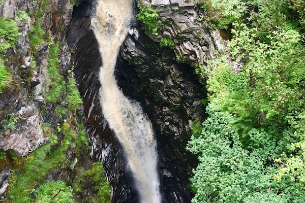 Ein Wasserfall stürzt über eine steile Felswand, umgeben von üppiger Vegetation.