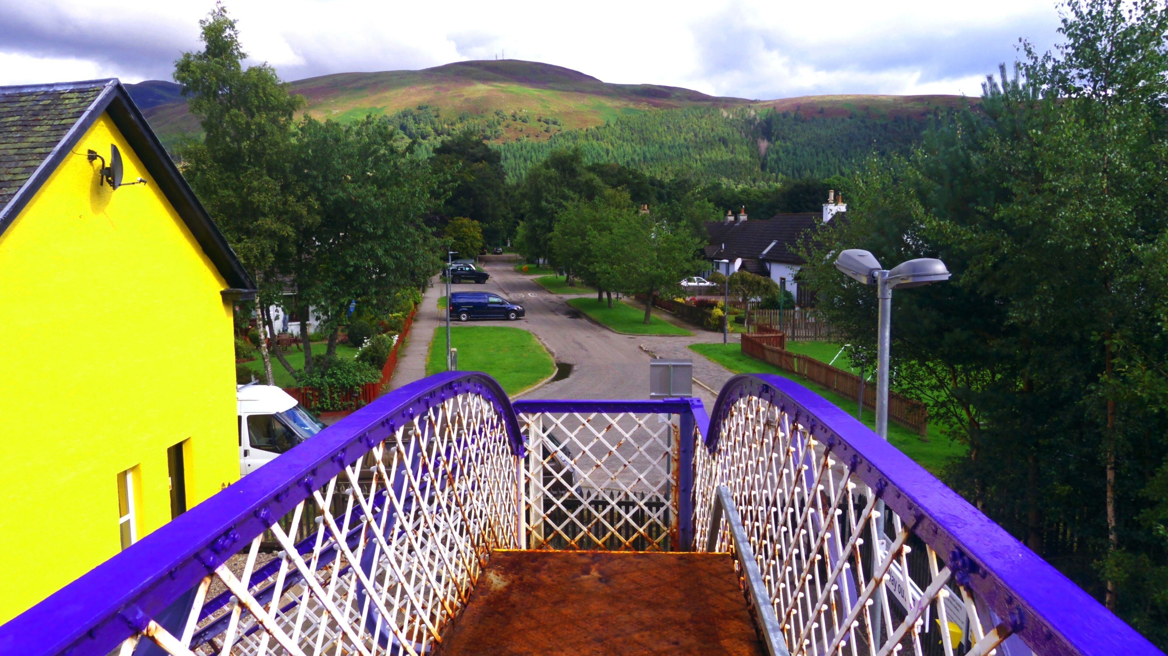A purple pedestrian bridge with a yellow building on the left.