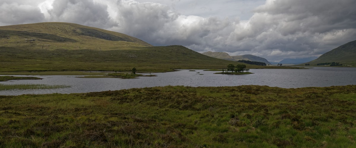 A lake surrounded by rolling hills and cloudy skies.