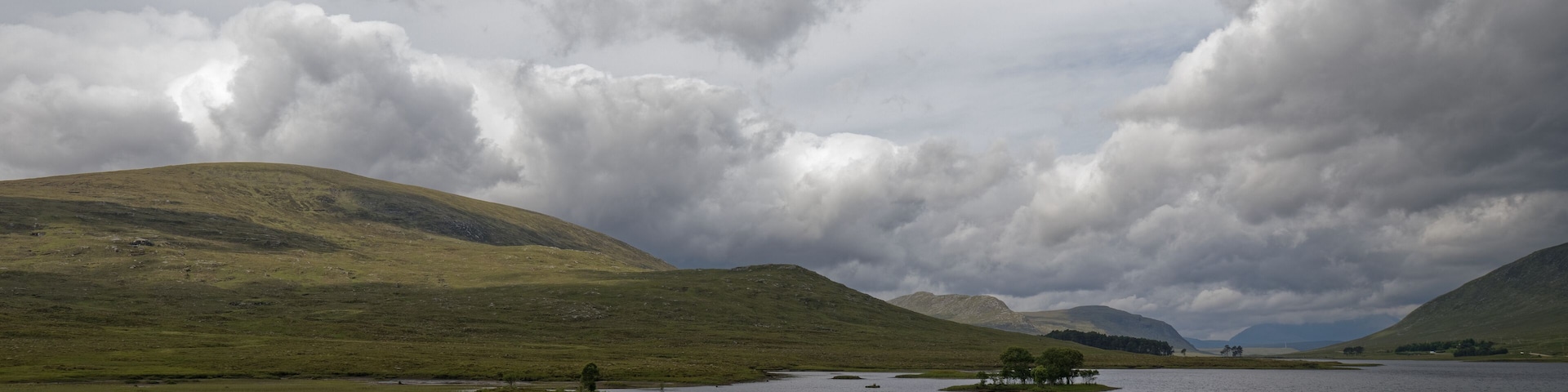 A lake surrounded by rolling hills and cloudy skies.