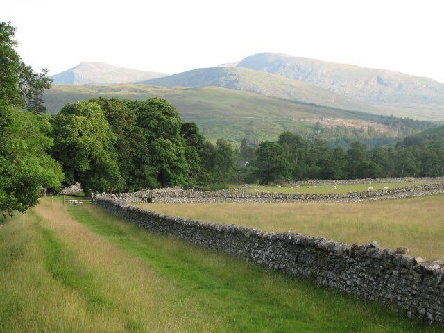 A stone wall, a grassy field, and a mountain range.