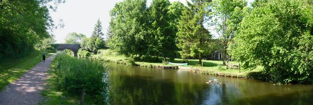 A calm river with a bridge, lush greenery, and a path.