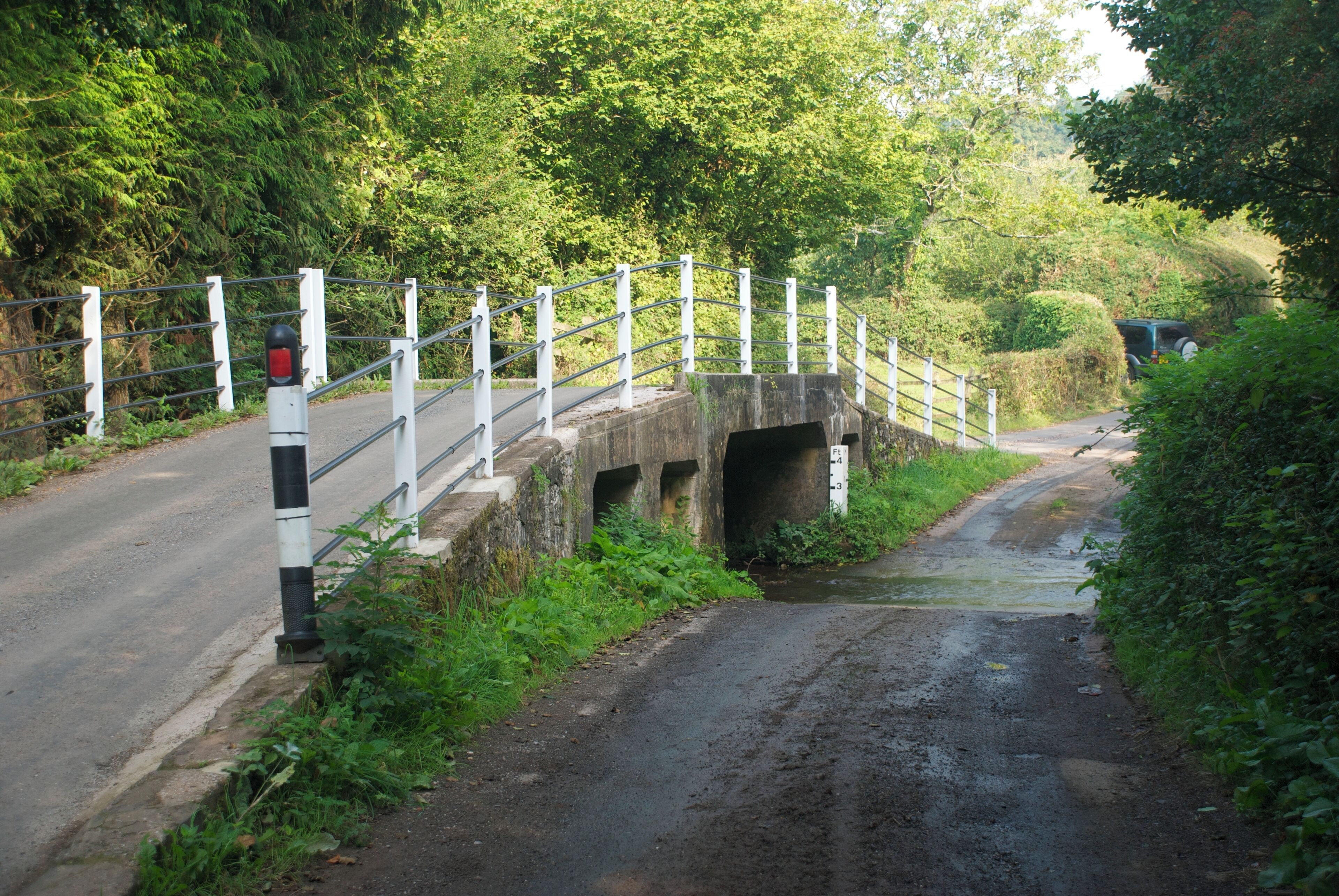 A narrow road passing under a stone bridge with metal railings and a red stop sign.