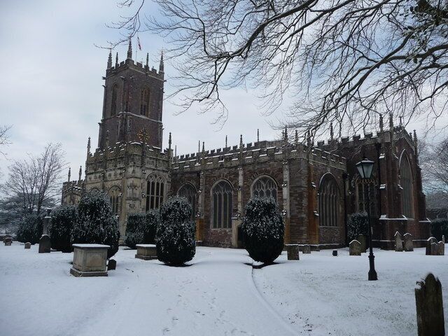 Una iglesia histórica con una alta torre y ventanas de arco, rodeada de árboles cubiertos de nieve y un cementerio.