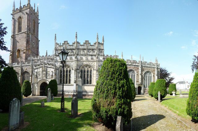 A historic cathedral with a tall tower, surrounded by well-maintained lawns and trimmed hedges.