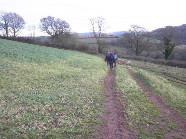 A group of hikers on a dirt path in a rural area with rolling hills and sparse trees.