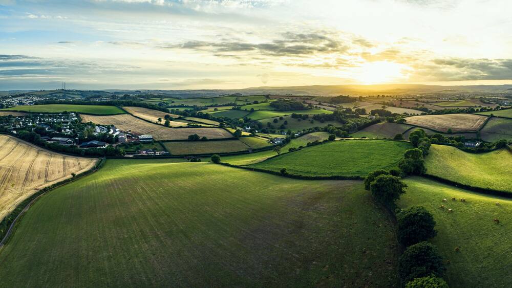Welliges Grün, ein Dorf und ferne Hügel unter einem Abendhimmel.