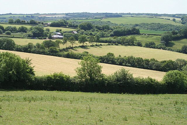Rolling green fields, a distant white house, and a hilly landscape.