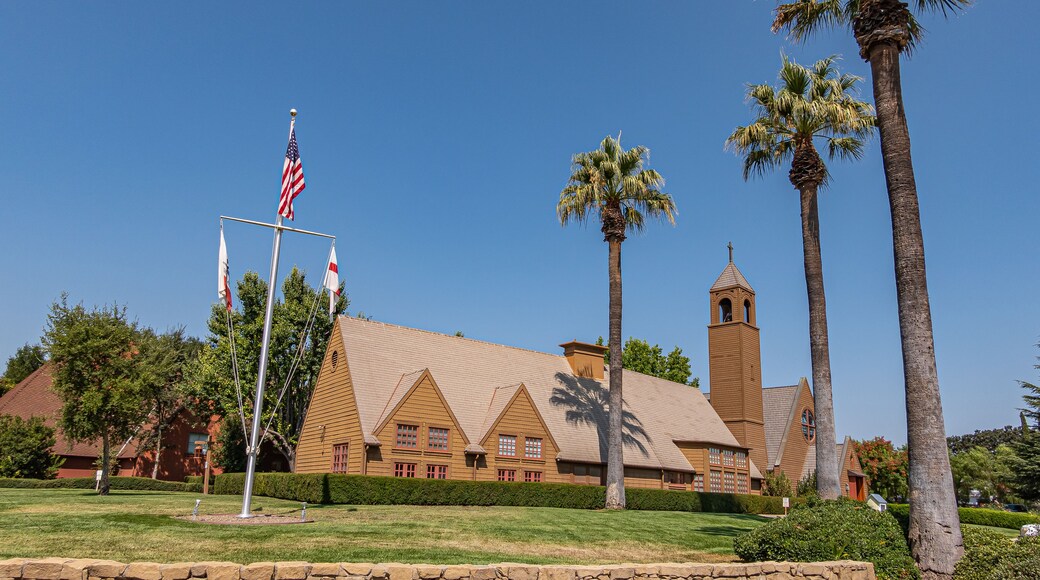 Los Olivos, California, USA - September 3, 2020: Wide view on brown wood St. Marks in the Valley Church with bell tower set in green park under blue sky, including side buildings. Flag post up front.