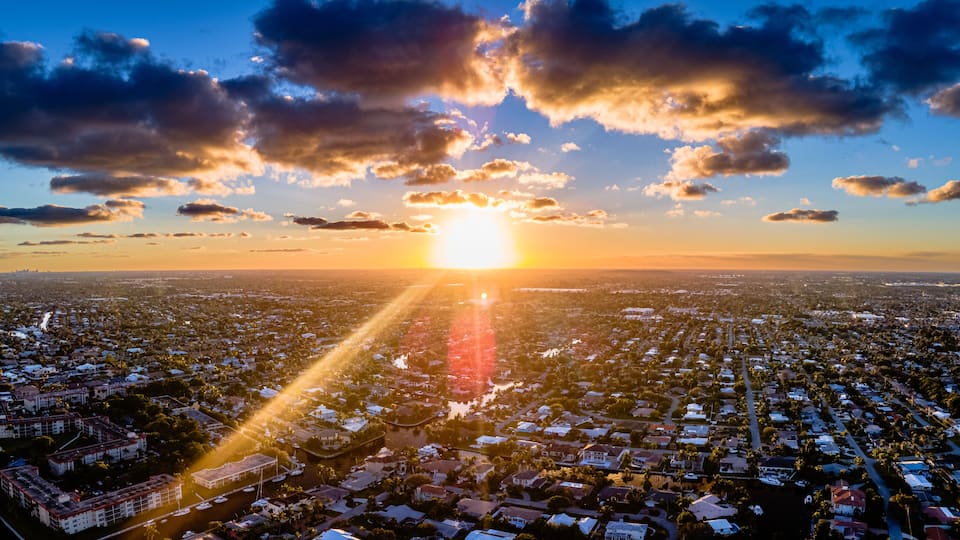 A cityscape at sunset with the sun low on the horizon, casting long shadows across the urban area.