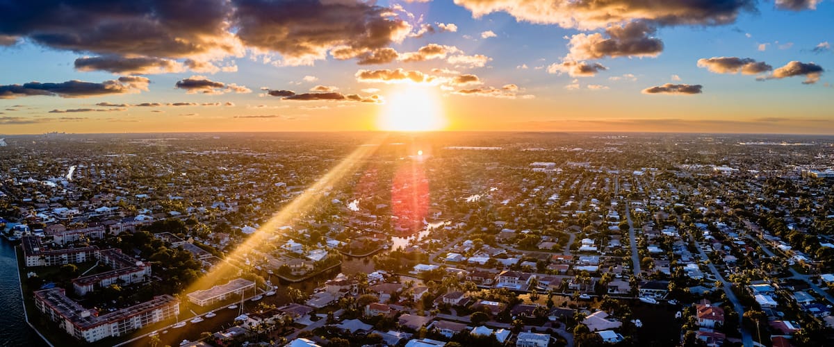 A cityscape at sunset with the sun low on the horizon, casting long shadows across the urban area.