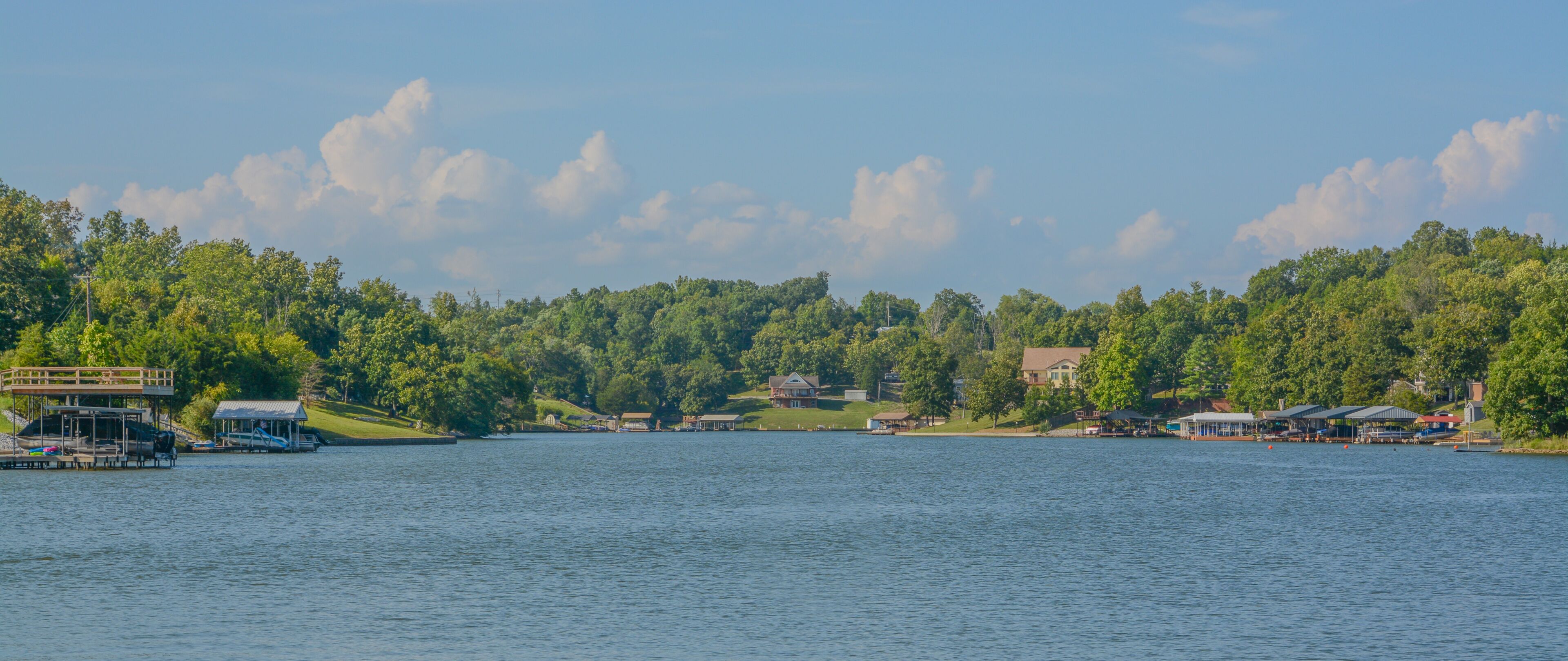 A lake with docked boats, a wooden pier, and houses surrounded by dense forest.