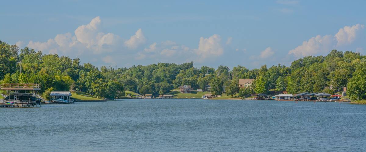 A lake with docked boats, a wooden pier, and houses surrounded by dense forest.