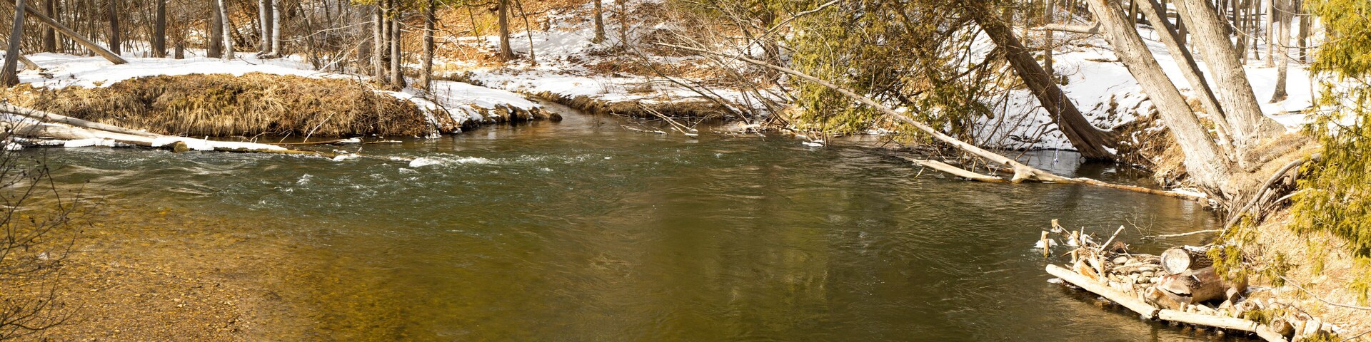 A river flowing through a forest with snow on the ground and trees.