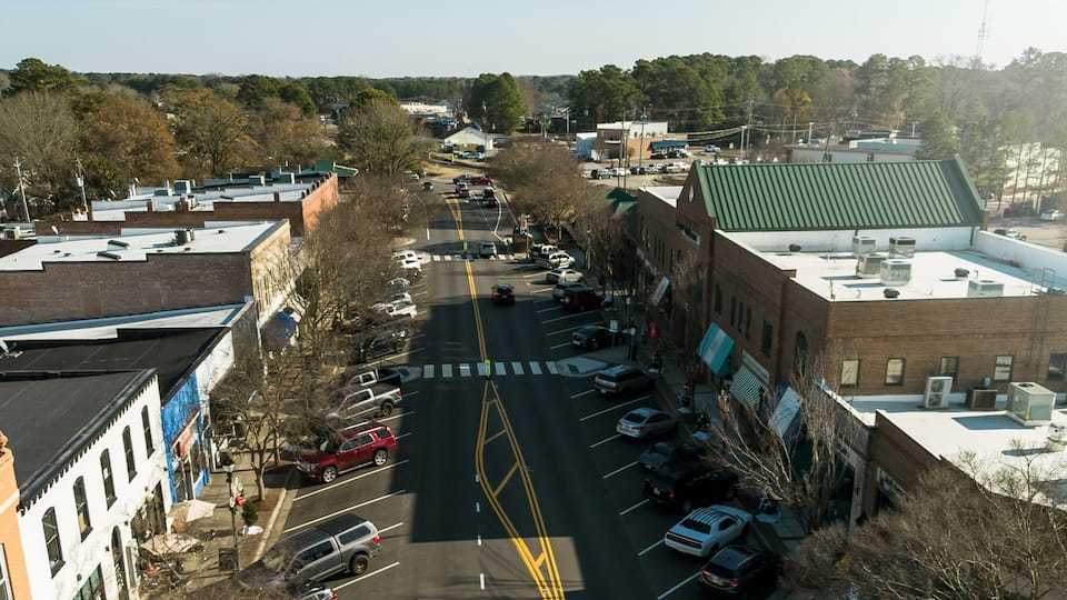 A wide street lined with parked cars, buildings, and trees.