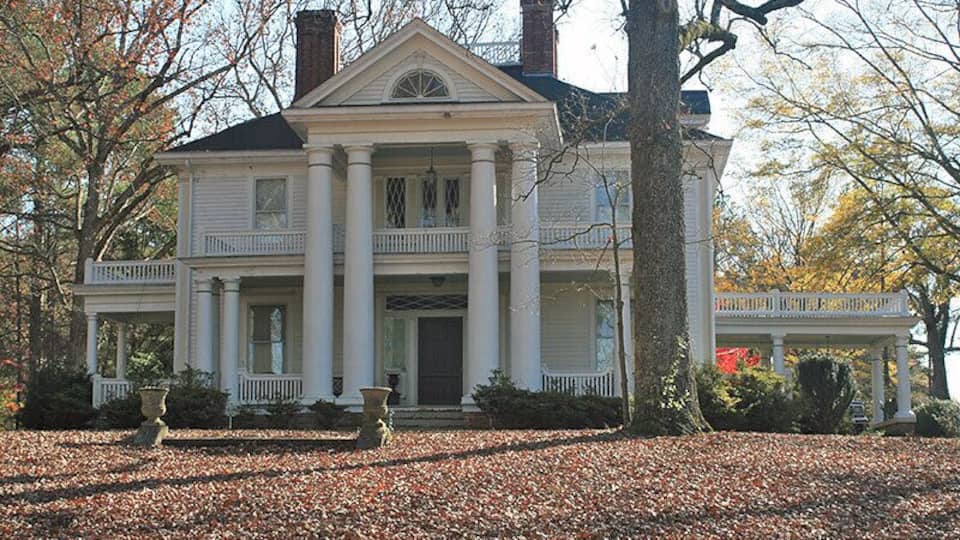 A large white colonial-style house with a central front door, two-story porch, and columns.