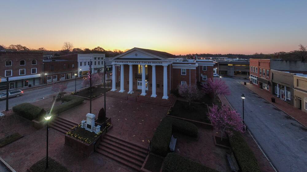 A courthouse with columns and a flag, surrounded by a landscaped area with trees and a street.