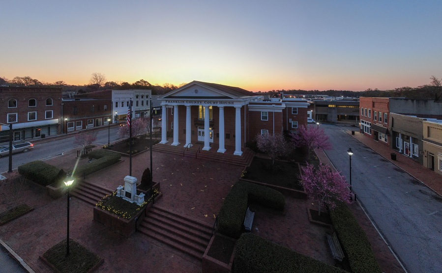 A courthouse with columns and a flag, surrounded by a landscaped area with trees and a street.