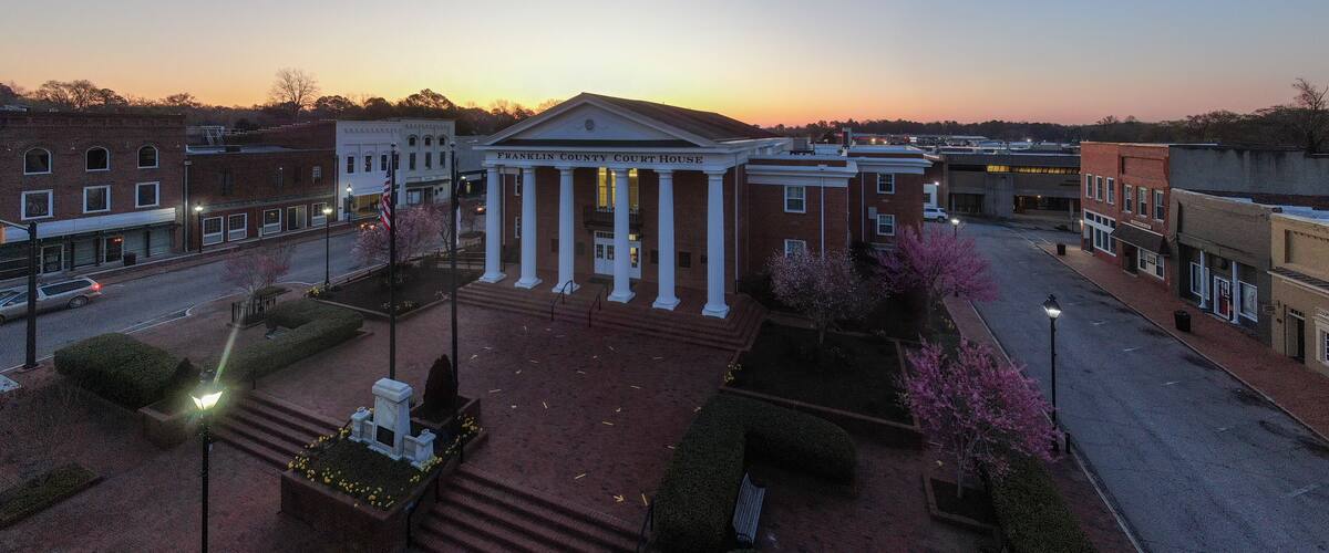 A courthouse with columns and a flag, surrounded by a landscaped area with trees and a street.