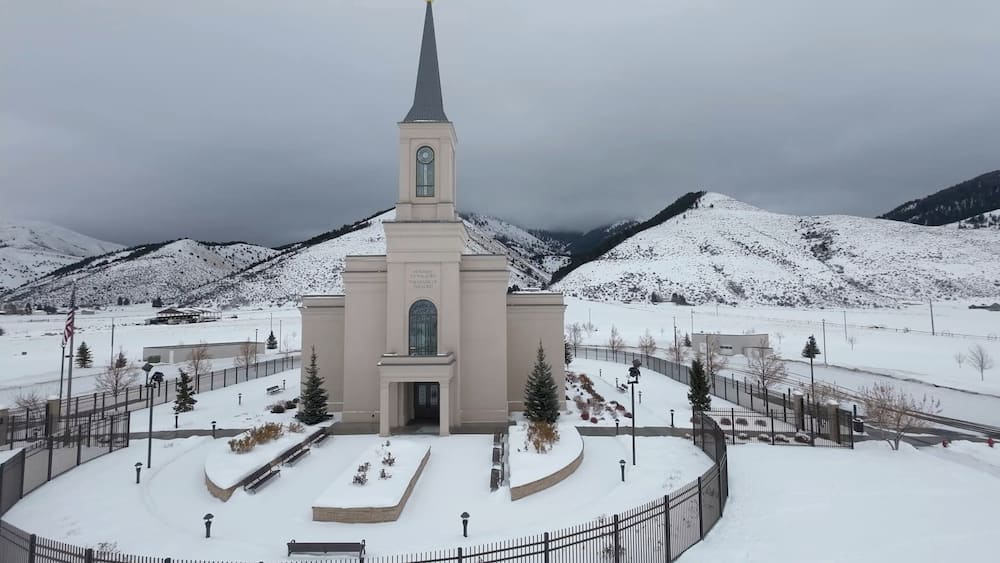 Une église dotée d’un clocher, entourée de montagnes enneigées et surplombant un ciel dégagé.