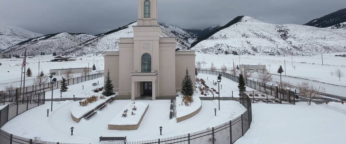 A church with a steeple, surrounded by snow-covered mountains and a clear sky.