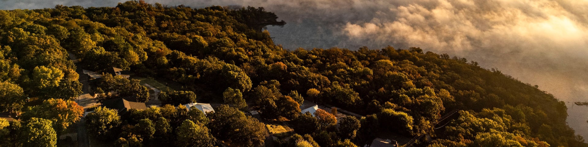A forested landscape with a river, mist-covered hills, and a small settlement.