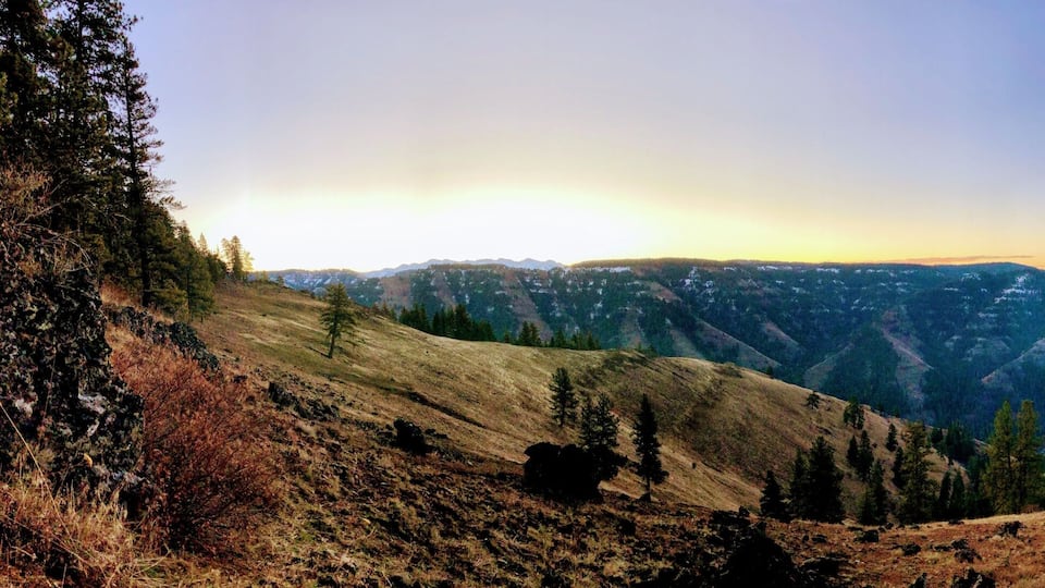 A mountainous landscape with a valley, trees, and a clear sky.
