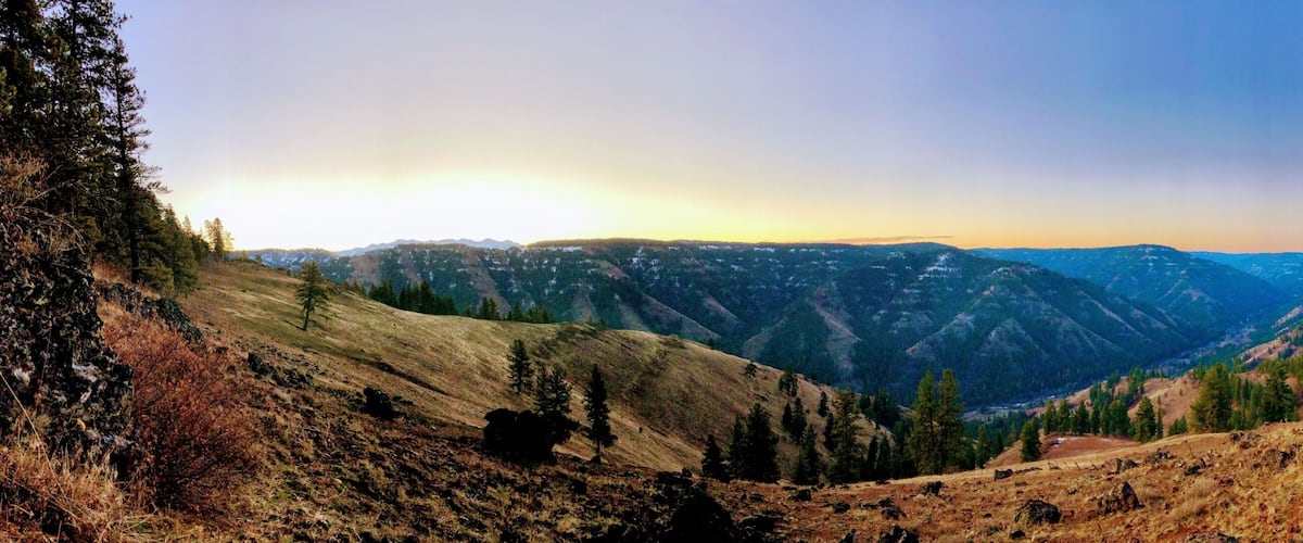 A mountainous landscape with a valley, trees, and a clear sky.