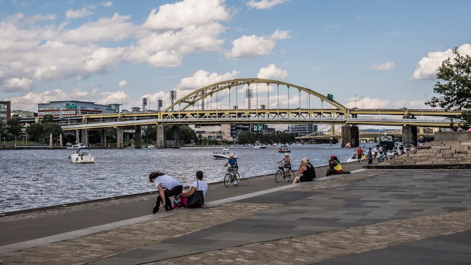 A river with boats, a pedestrian walkway, and a bridge in the background.