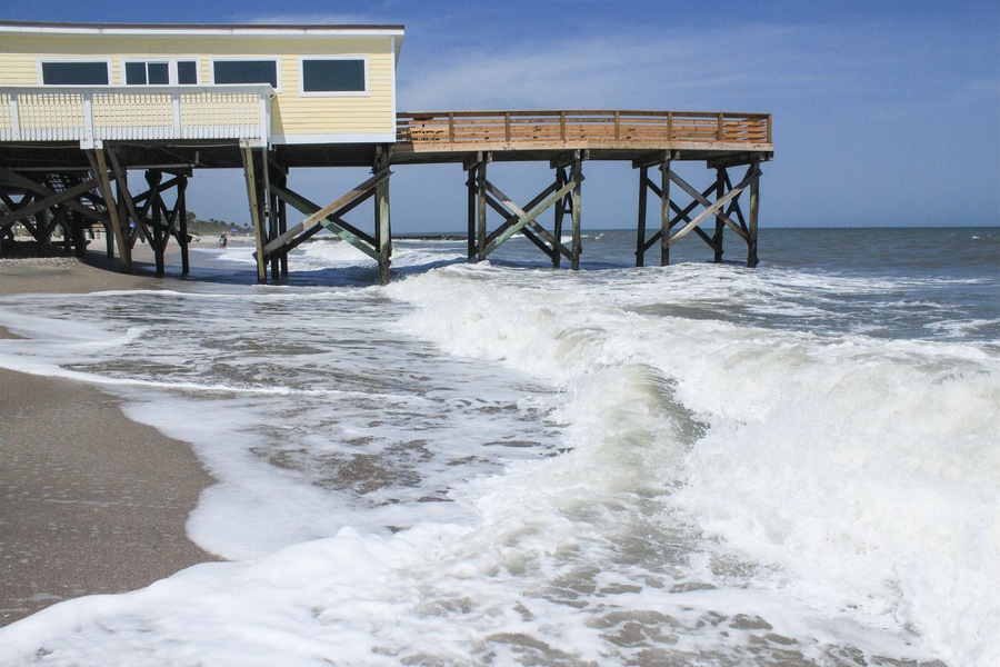 A wooden pier extending into the ocean with a building on the left.