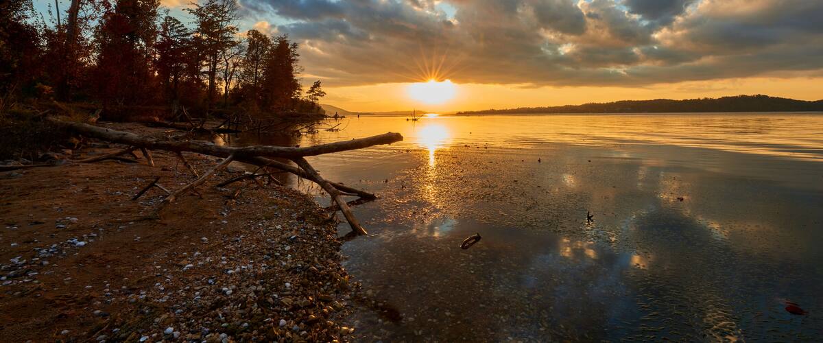 A sunset over a calm lake with trees and a rocky shoreline.
