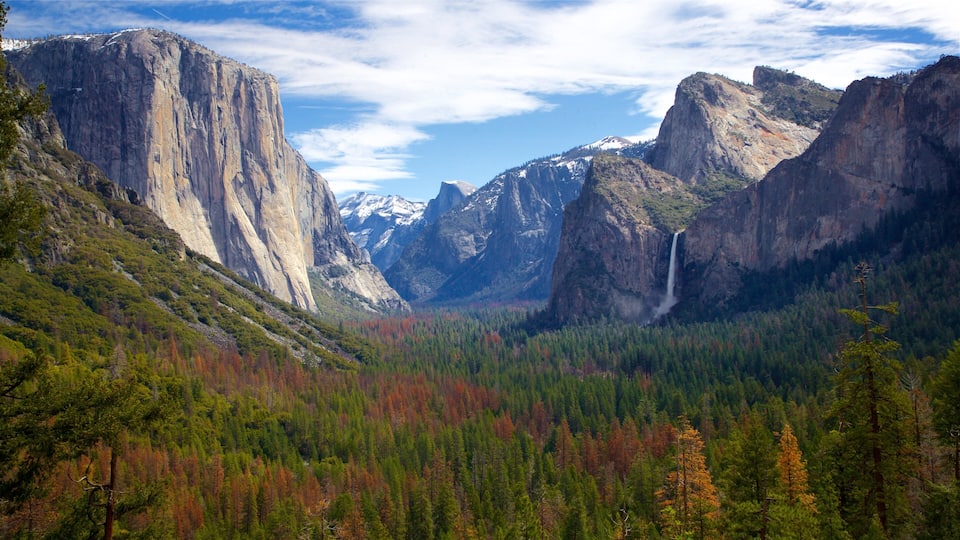 A mountainous landscape with a prominent rock face, a waterfall, and a forested valley.