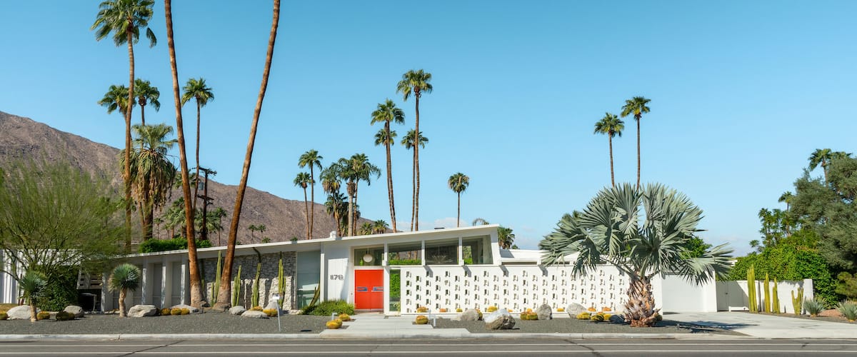 A building with a red door, surrounded by palm trees and cacti.