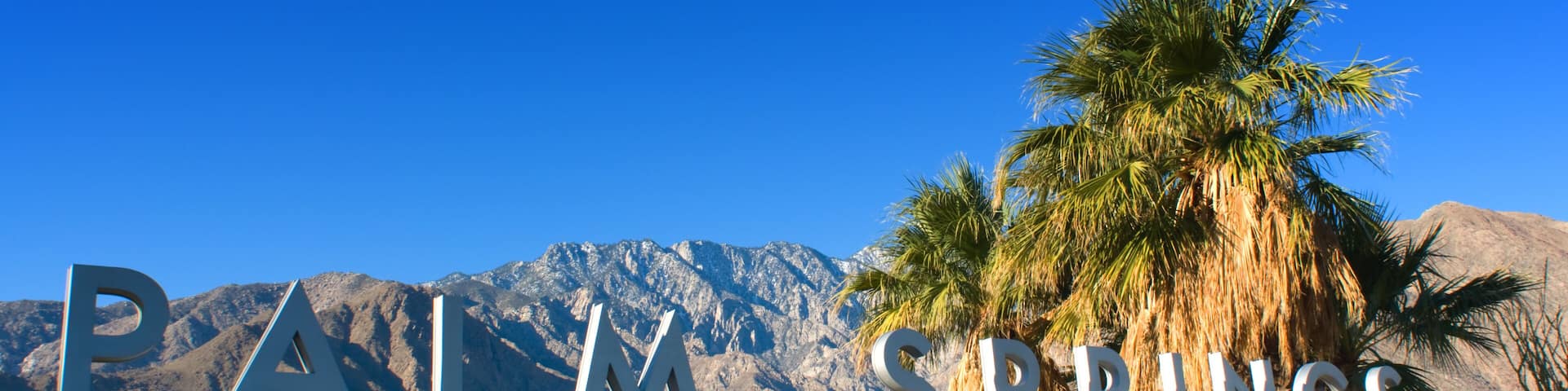 A sign reading "PALM SPRINGS" with palm trees and mountains in the background.