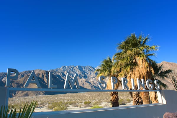 A sign reading "PALM SPRINGS" with palm trees and mountains in the background.