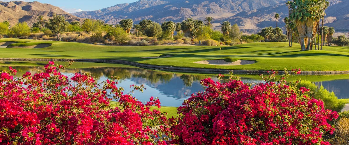 A golf course with a lake, palm trees, and mountains in the background.