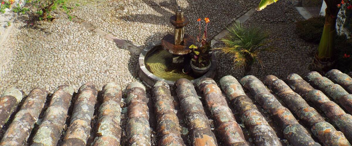 A courtyard with a fountain, tiled roof, and potted plants.