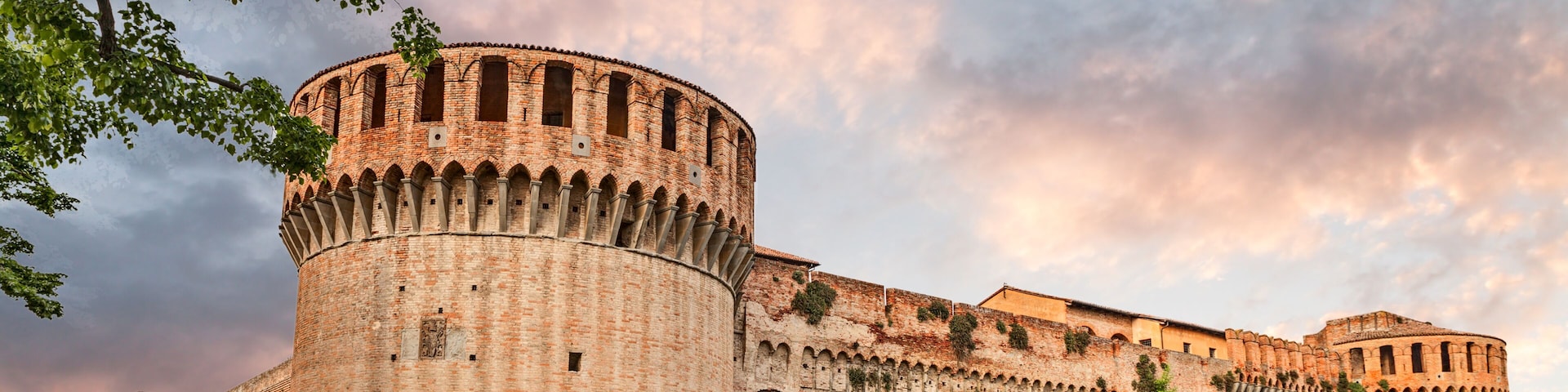 Una fortaleza histórica de ladrillo con una torre redonda, ventanas en arco y una gran entrada.