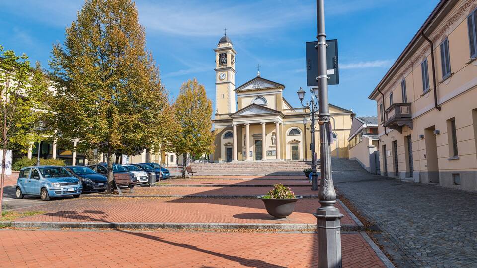 A historic church with a clock tower, parked cars, and a cobblestone street.