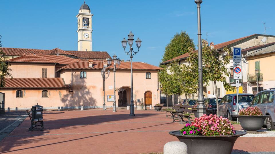 A plaza with a clock tower, benches, street lamps, and flower planters.