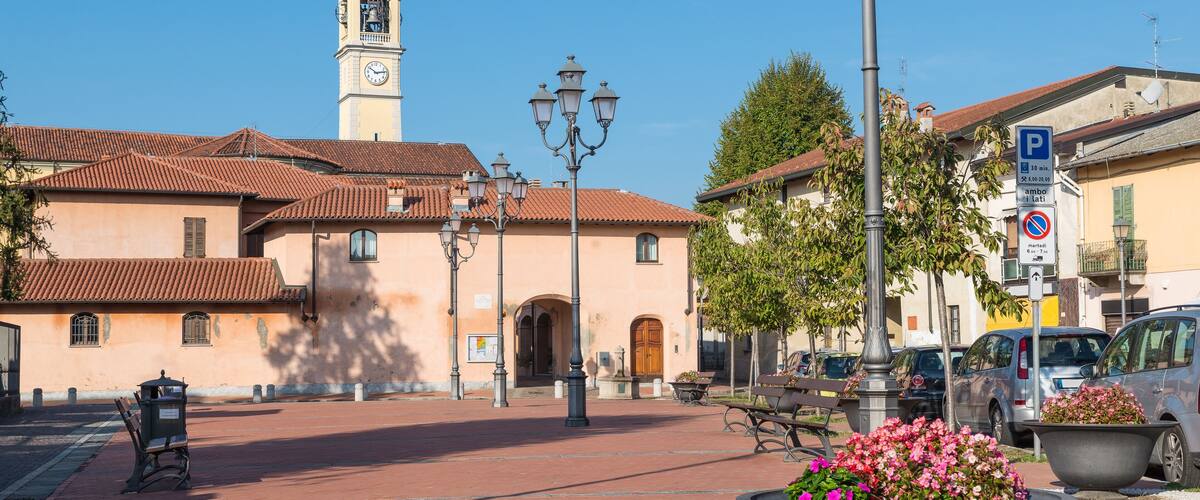 A plaza with a clock tower, benches, street lamps, and flower planters.