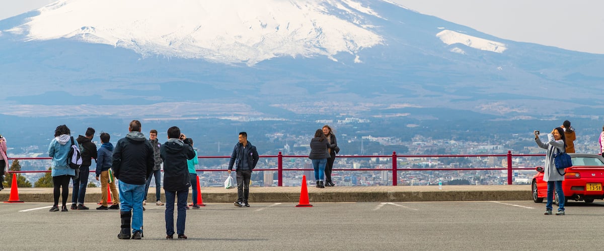 A group of people standing on a viewing platform with a snow-capped mountain in the background.