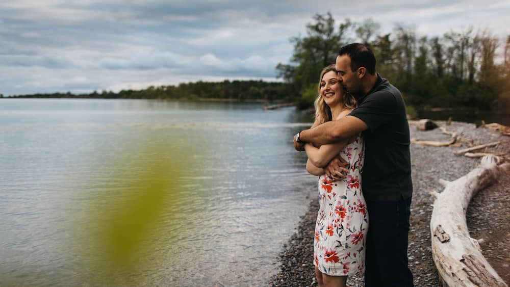 Un couple s’embrasse au bord d’un lac, avec une forêt en arrière-plan.