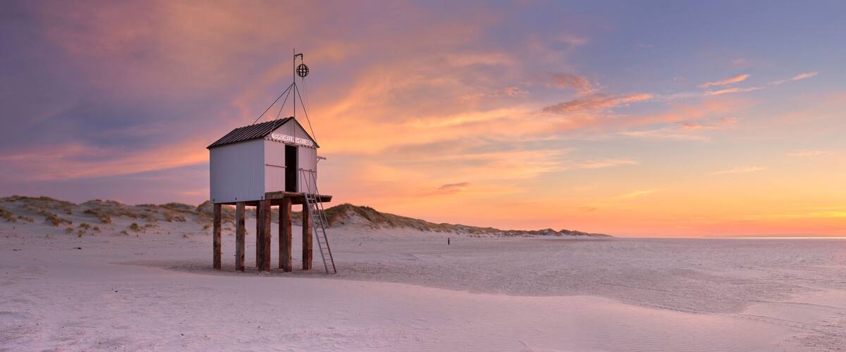 A beach hut with a flagpole and a sunset in the background.