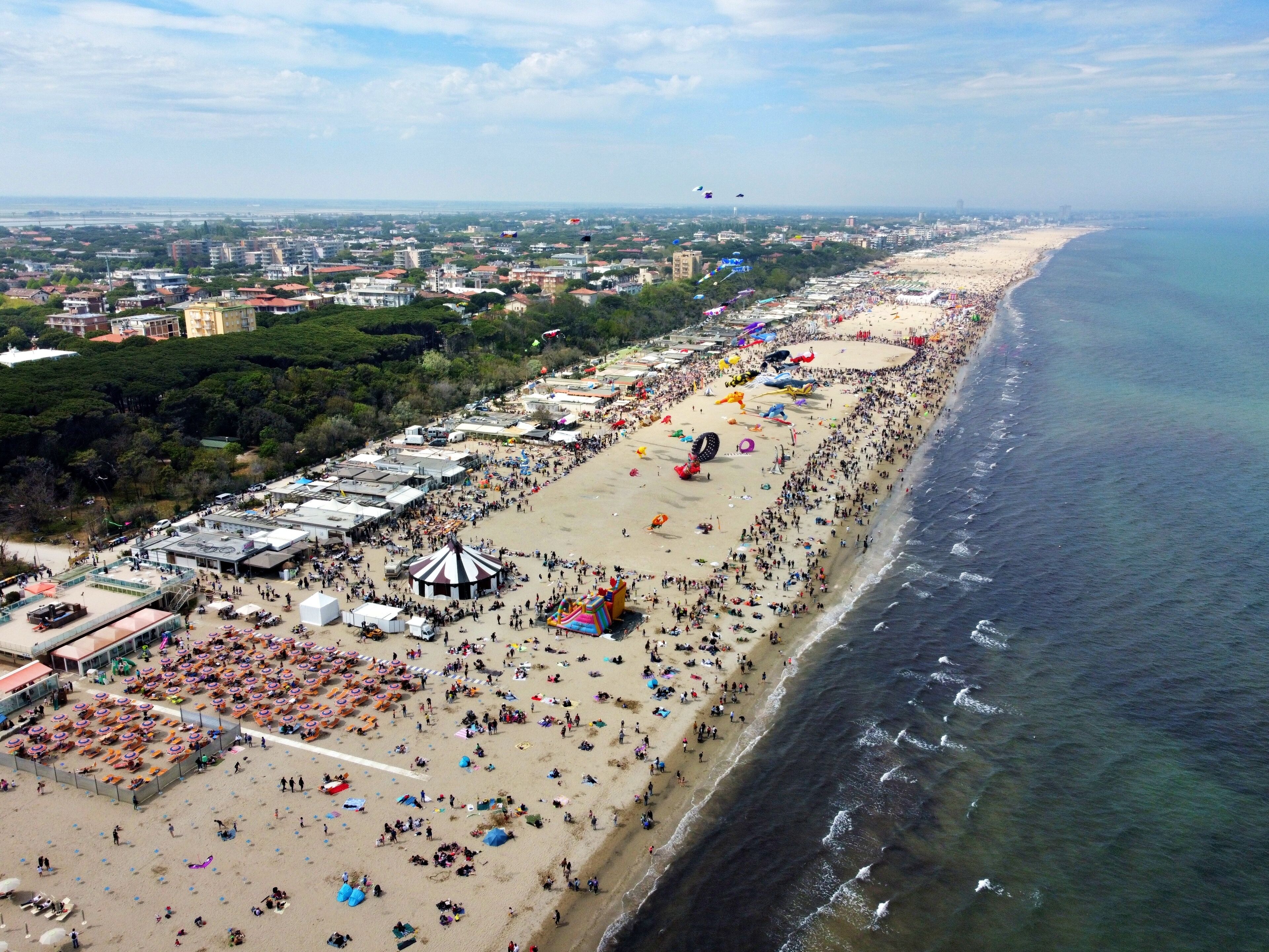 A crowded beach with numerous umbrellas and tents, a large crowd of people, and a clear view of the ocean.